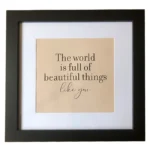 Square black photo frame with a beige insert featuring the message 'The world is full of beautiful things... like you' in elegant typography.