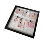Black frame with grid backing displayed as an earring organizer, featuring various colorful earrings clipped on pink cards.