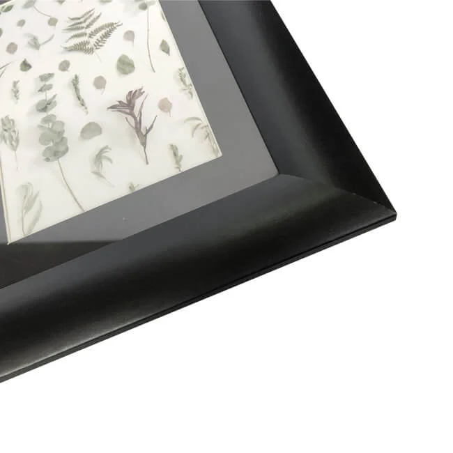 A sleek black photo frame displaying a botanical artwork featuring pressed leaves and floral elements on a white background.
