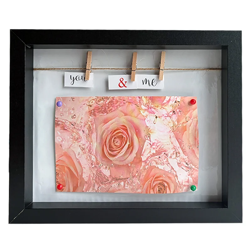 Black photo frame featuring pink roses and a 'You & Me' message on clothespins, creating an elegant and romantic display.