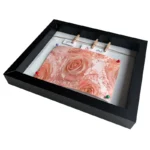 Black shadow box photo frame displaying a pink floral card pinned with colorful pins and wooden clips on a twine.