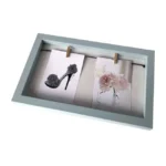 Gray wooden photo frame featuring a high-heeled shoe drawing and a pink flower artwork clipped to strings.