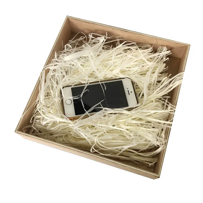A smartphone resting securely in a box filled with white shredded paper for protective packaging.