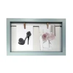 A light blue photo frame displaying two art prints, one of a floral high heel and one of pink flowers in a vase, held by clips.