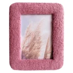 A pink textured photo frame with a soft, fuzzy surface, enclosing an artistic image of dried grass against a light background.