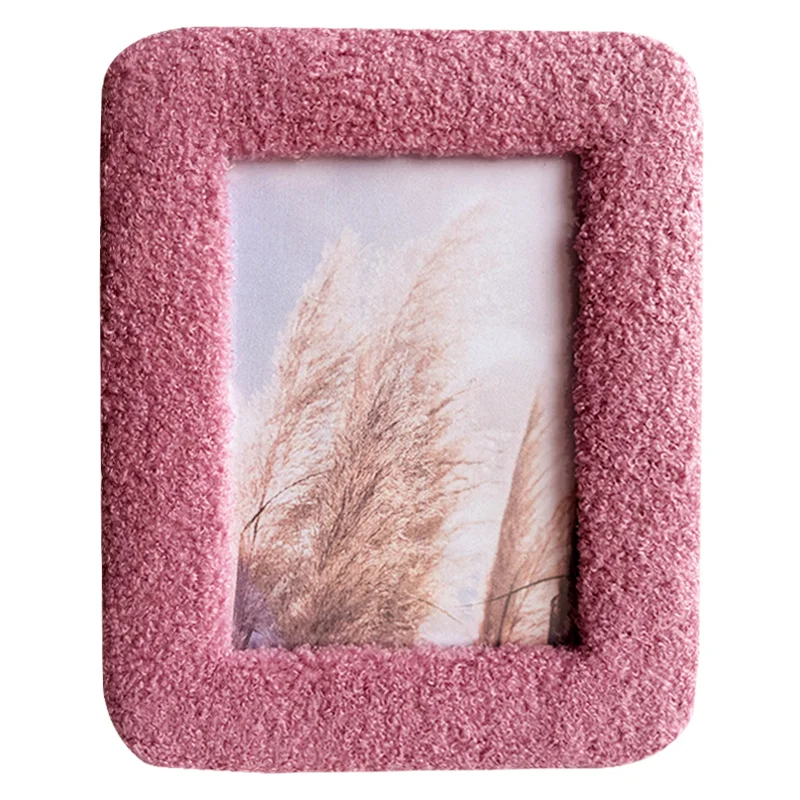A pink textured photo frame with a soft, fuzzy surface, enclosing an artistic image of dried grass against a light background.