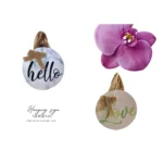 Two round decorative hanging signs featuring 'hello' on a marble design and 'love' on a wooden design, adorned with rustic burlap bows, accompanied by a purple orchid flower.