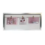 A silver frame featuring a white background and a horizontal string with clips holding three pieces of pink-toned artwork.