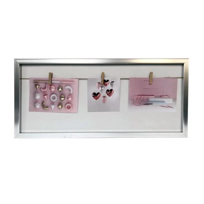 A silver frame featuring a white background and a horizontal string with clips holding three pieces of pink-toned artwork.
