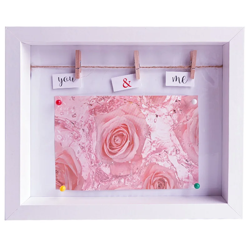 White photo frame displaying pink rose artwork, clipped notes reading 'you & me,' and colorful push pins.