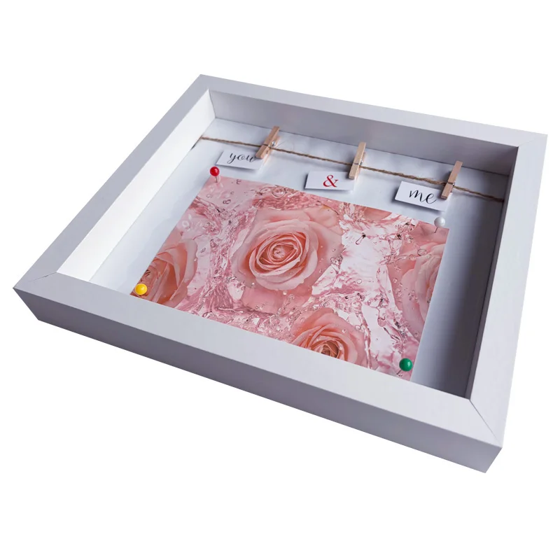 White shadow box photo frame holding a decorative card of pink roses and small clips with text 'you & me'.