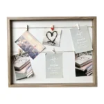 A wooden photo collage frame featuring multiple photos and quotes clipped with small pegs on strings.