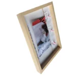 Angled view of a light wooden photo frame displaying a decorative design with a photo, text cards, and pink clips.
