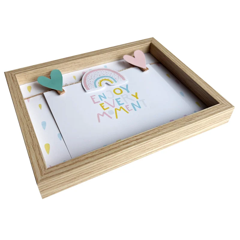 Rectangular wooden photo frame with colorful rainbow and heart-shaped clips holding a card that says 'Enjoy every moment'.