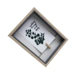 Wooden shadow box photo frame displaying a botanical print and decorative text, held by a small clip, on a white background.